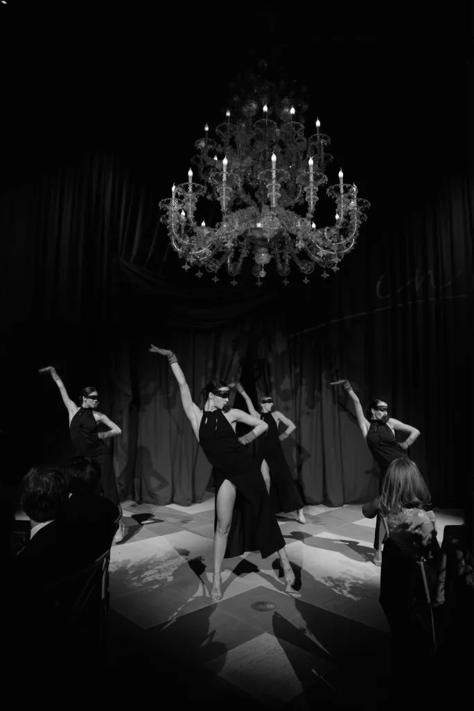 Masked dancers performing under a chandelier